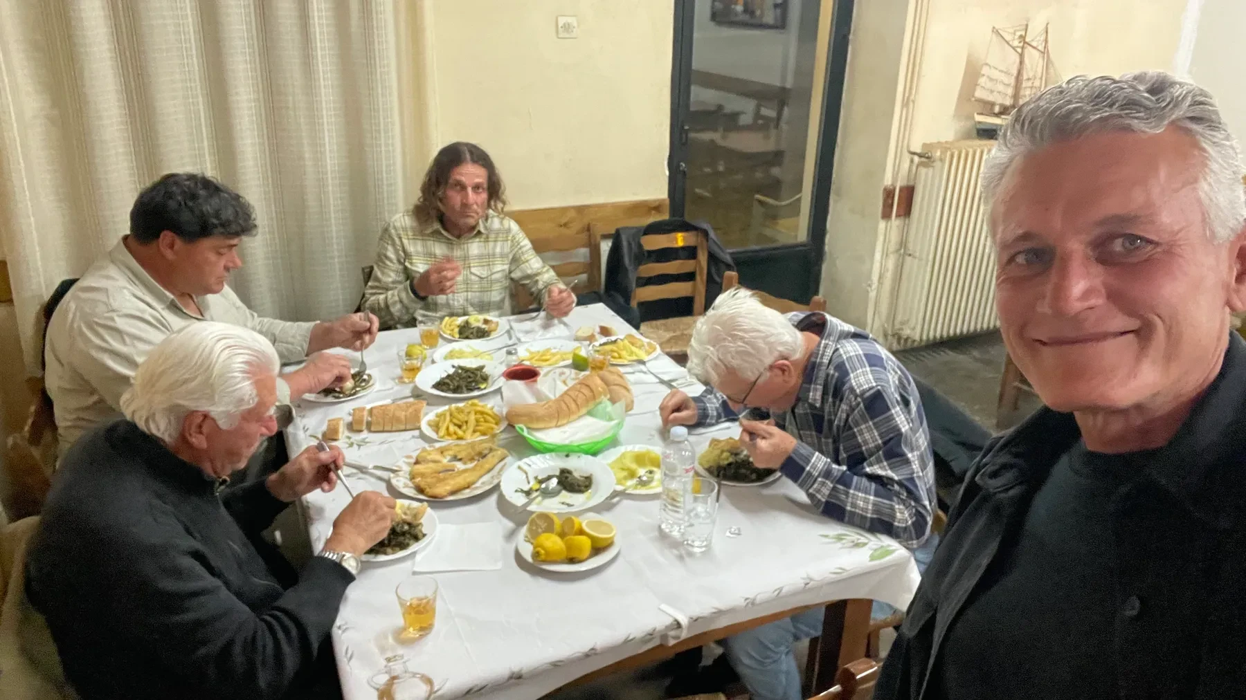 Ευάγγελος (Angelo), Βασίλης (Vasili), Αλέξανδρος (Alexandros), and Νικόλαος (Nick) at a taverna, with Κωνσταντίνος (Konstantinos) behind the camera