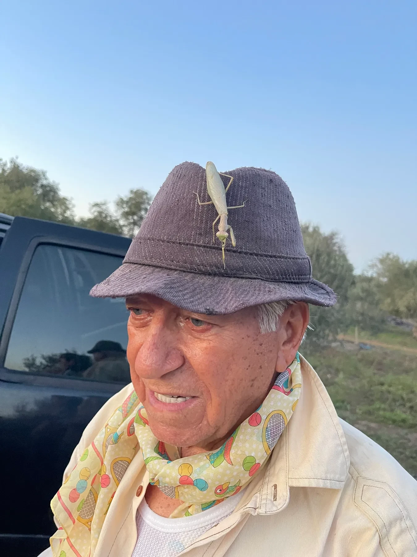 Ευάγγελος (Angelo) smiling, a praying mantis resting on the brim of his cap