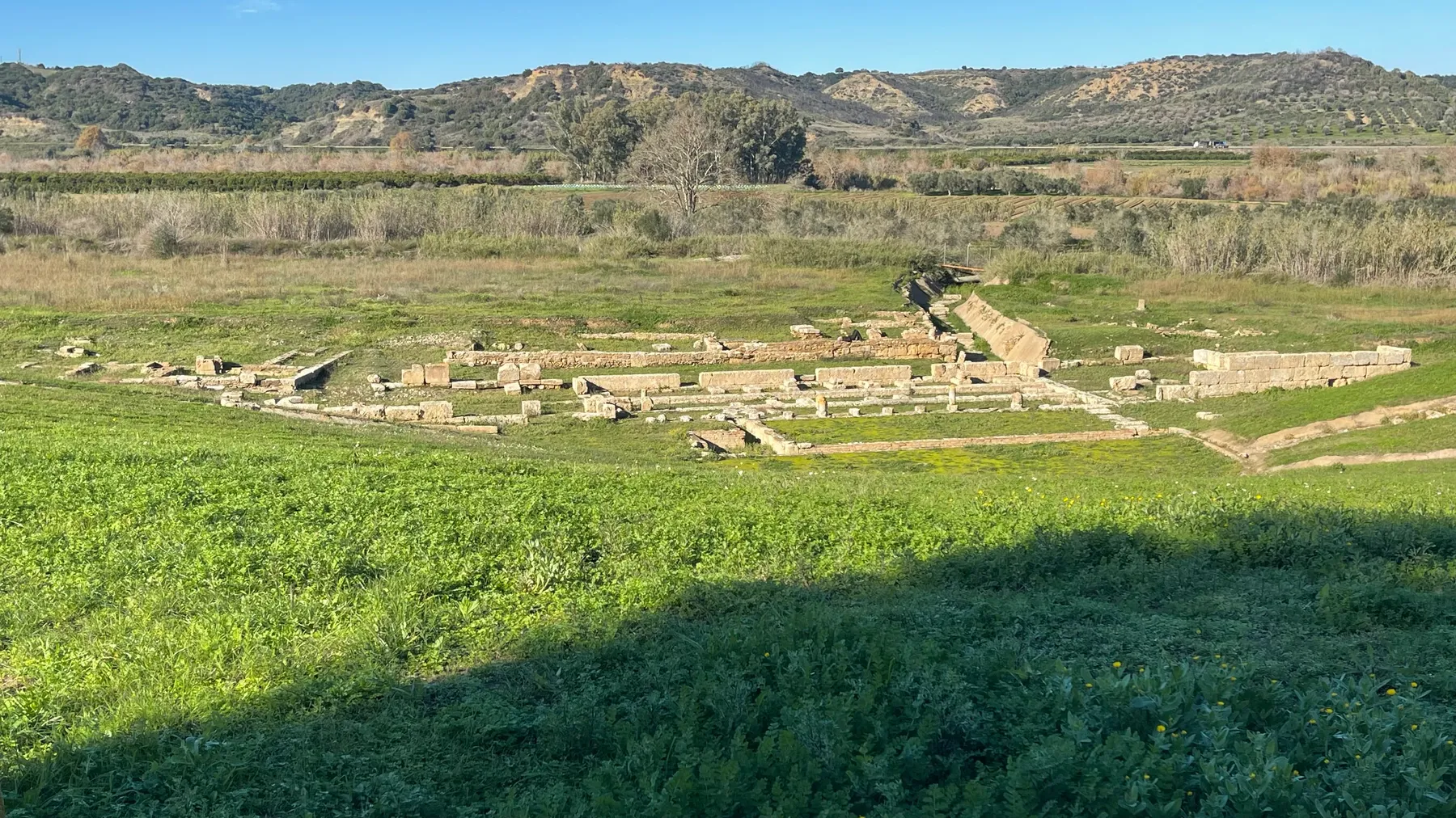 A wide view across the theatre ruins at Ancient Elis, hills in the distance