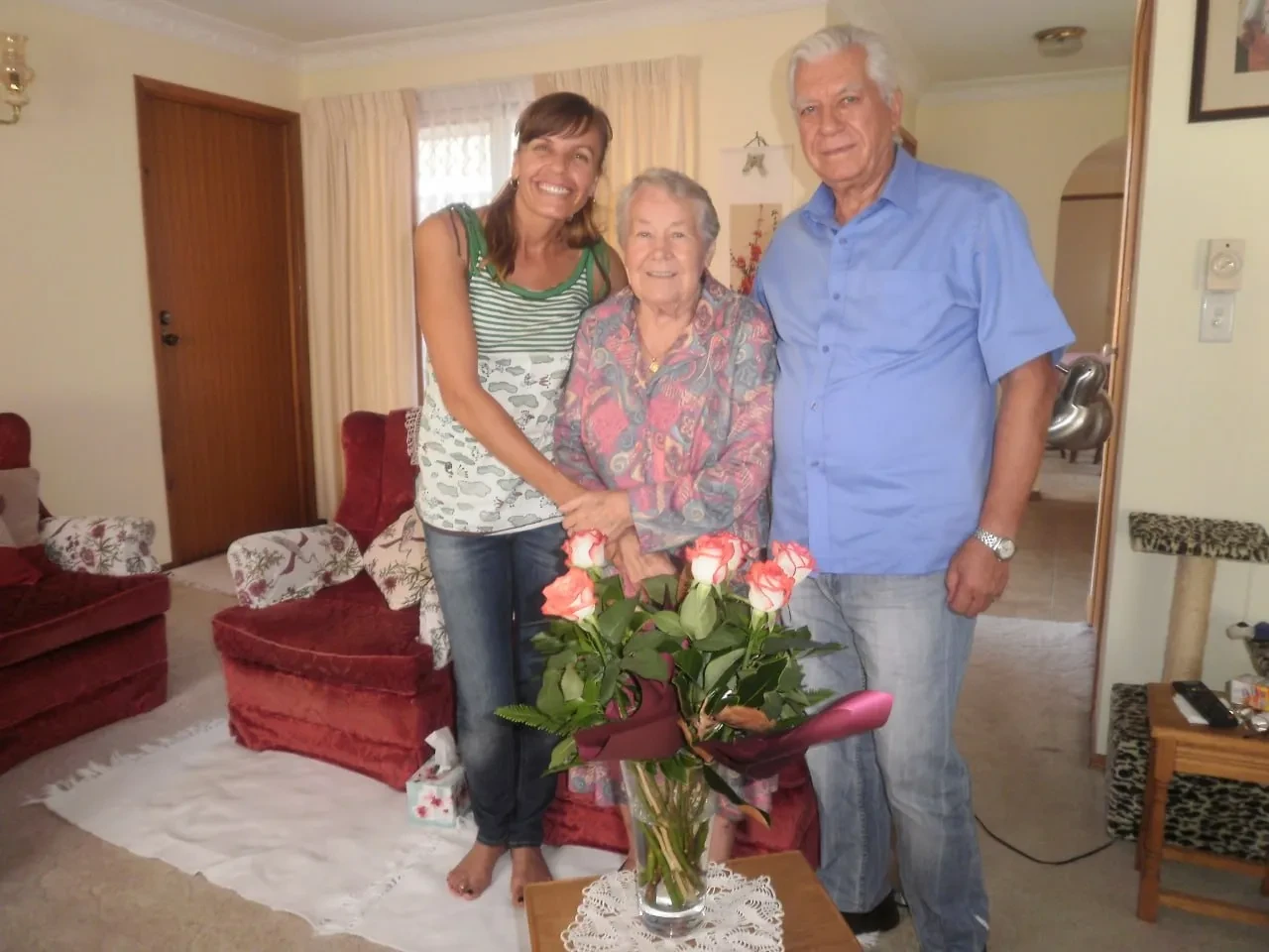 Ευαγγελία (Evangelia), Henryka, and Ευάγγελος (Angelo) together at home, roses on the table