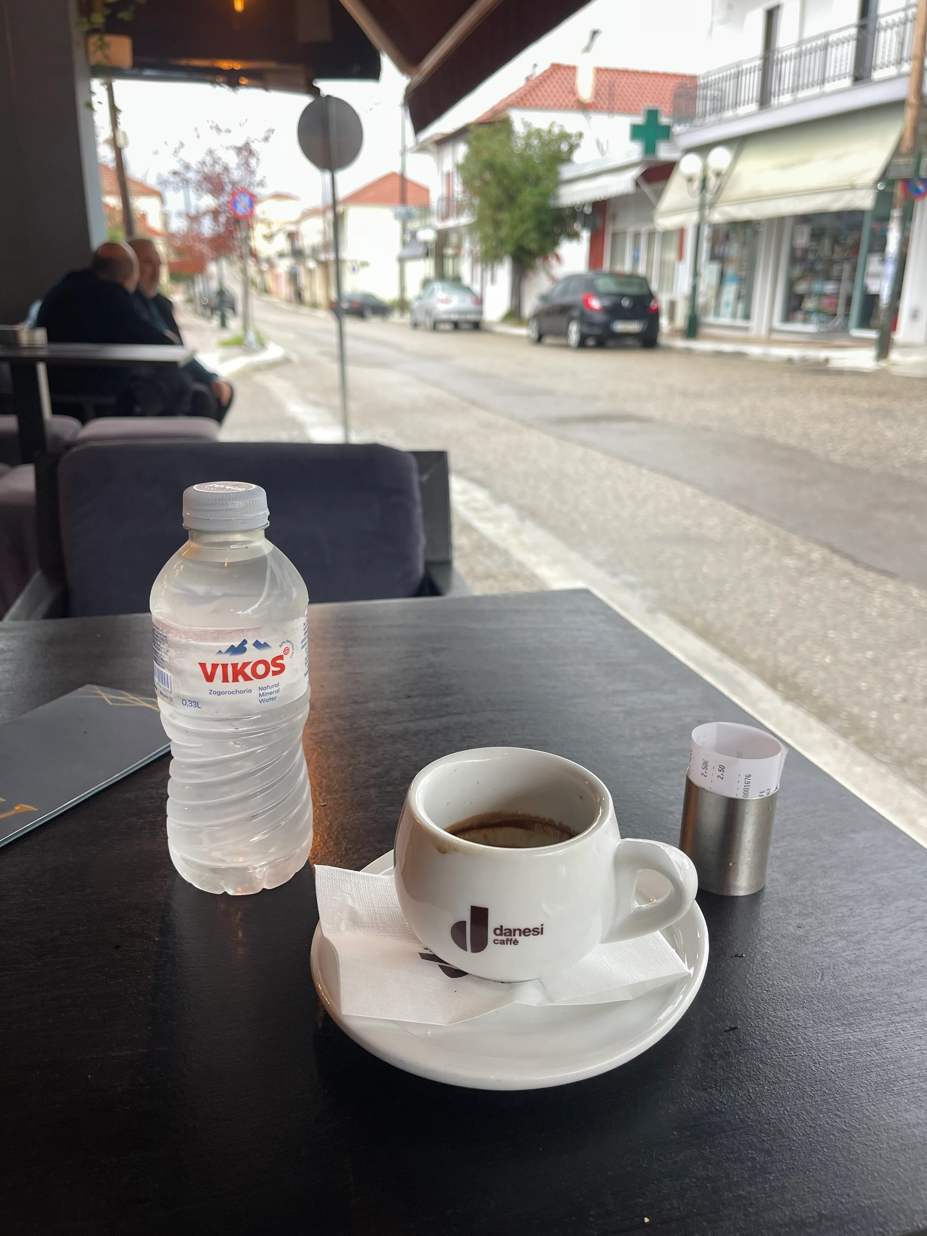 A Greek coffee and a small bottle of water on a café table on the main street of the village